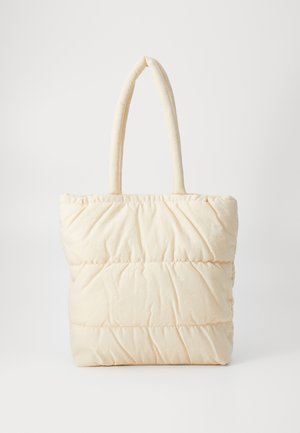 Puffet tote bag i kremfarge, med myk stoff, firkantet form og to polstrede håndtak. Synlige sømmer gir tekstur.