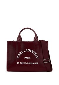 Burgundy leather tote bag with dual top handles, adjustable shoulder strap, white printed text, structured silhouette, smooth texture.