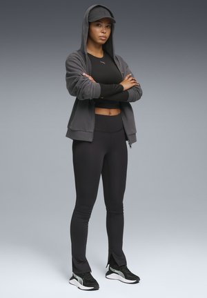 Czarna sportowa koszulka, szara bluza z kapturem zapinana na zamek, czarne legginsy i czarne trampki. Strój ma kaptur i subtelne detale szwów.