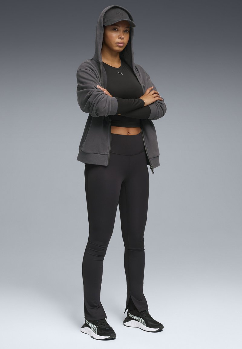 Czarna sportowa koszulka, szara bluza z kapturem zapinana na zamek, czarne legginsy i czarne trampki. Strój ma kaptur i subtelne detale szwów.