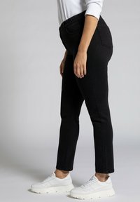 Black denim jeans with a slim fit, featuring a stretchy waistband and standard pockets, paired with white athletic shoes.