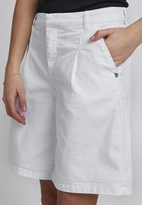 Hvide bomuldsshorts med en afslappet pasform, der har sidelommer og et lille dekorativt emblem foran nær hoften.
