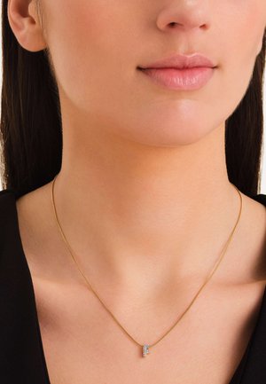 Złoty naszyjnik z łańcuchem z małym, eleganckim zawieszką w kształcie litery, ozdobioną przezroczystymi kamieniami szlachetnymi, charakteryzujący się gładkim wykończeniem i minimalistycznym wzornictwem.