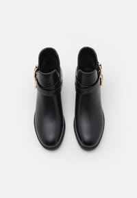 Botas de cuero negro hasta el tobillo con una textura suave, puntera redondeada y un acento de hebilla en tono dorado en la correa del tobillo. Diseño de suela plana.