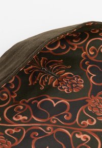 Καφέ καπέλο από κοτλέ με περίπλοκο μοτίβο εσωτερικής επένδυσης από πορτοκαλί καρδιές και κώνους σε σκούρο πράσινο φόντο, με ορατά ράμματα.