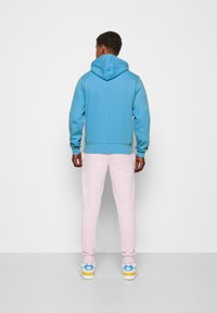 Hoodie in lichtblauw, gemaakt van zacht materiaal, gecombineerd met roze sweatpants en casual sneakers met blauwe en gele accenten.