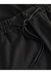Czarne spodnie dresowe wykonane są z fakturowanej tkaniny, mają regulowany pas ze sznurkiem oraz ozdobny guzik z przodu.