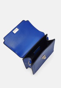 Blå läderaxelväska med guldspänne, öppen och visar svart insida samt rektangulärt metalldekor på insidan av klaffen.