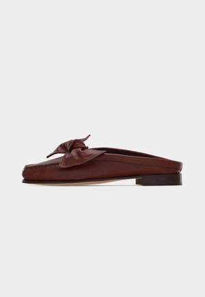 Barna bőr bebújós mokaszin alacsony sarokkal és nagy masni díszítéssel a tetején, oldalnézetben fehér háttéren.