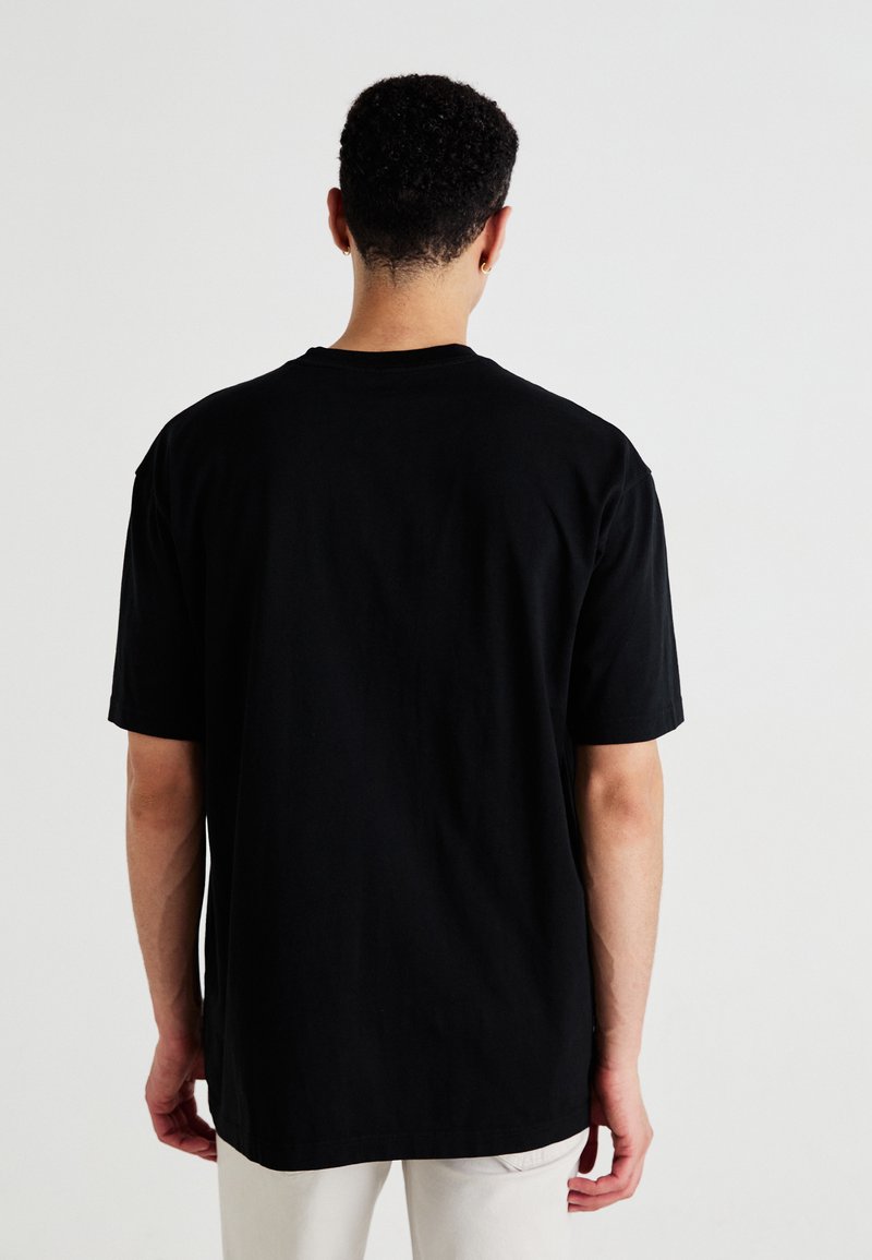 Czarna bawełniana koszulka z krótkim rękawem, okrągłym dekoltem i luźnym krojem, widoczna z tyłu. Gładka faktura, bez widocznych wzorów ani akcentów.