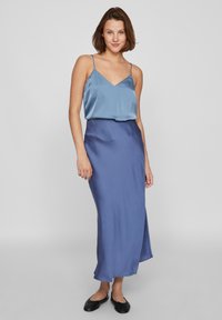 Camisole en satin bleu clair avec des bretelles fines, associée à une jupe maxi ajustée assortie avec une fente sur le côté. Texture lisse, silhouette élégante.