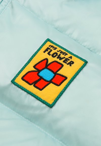 Kollane laim rohelist äärt helel kangal, kujutamas stiliseeritud punast ja sinist lille ning teksti "IT'S JUST A FLOWER."