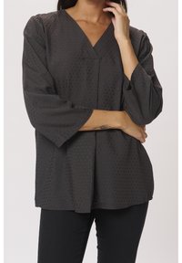 Tmavě šedá blůza s výstřihem ve tvaru V, tříčtvrtečními rukávy, jemnými tečkovanými vzory a volným střihem. Měkká látka s mírným leskem.