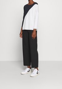 Top a blocchi bianchi e blu navy con maniche lunghe, abbinato a pantaloni neri larghi e sneakers bianche con dettagli neri.
