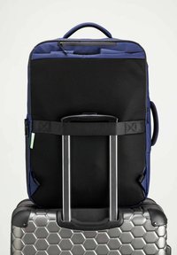 Marinblå ryggsäck med en texturerad svart mesh-bak, anpassad över en silvergrå resväska med hexagonmönster och dubbla kromhandtag.