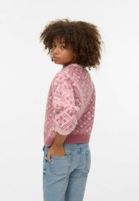 Rozā adīts džemperis ar ģeometrisku rakstu, apaļu kakla izgriezumu un nedaudz pūstām piedurknēm, kopā ar zilajām džinsām. Mīksta tekstūra.