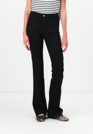 Black flared jeans with a high waist, featuring two front pockets and a copper button detail. Worn with a striped top and animal-print shoes.