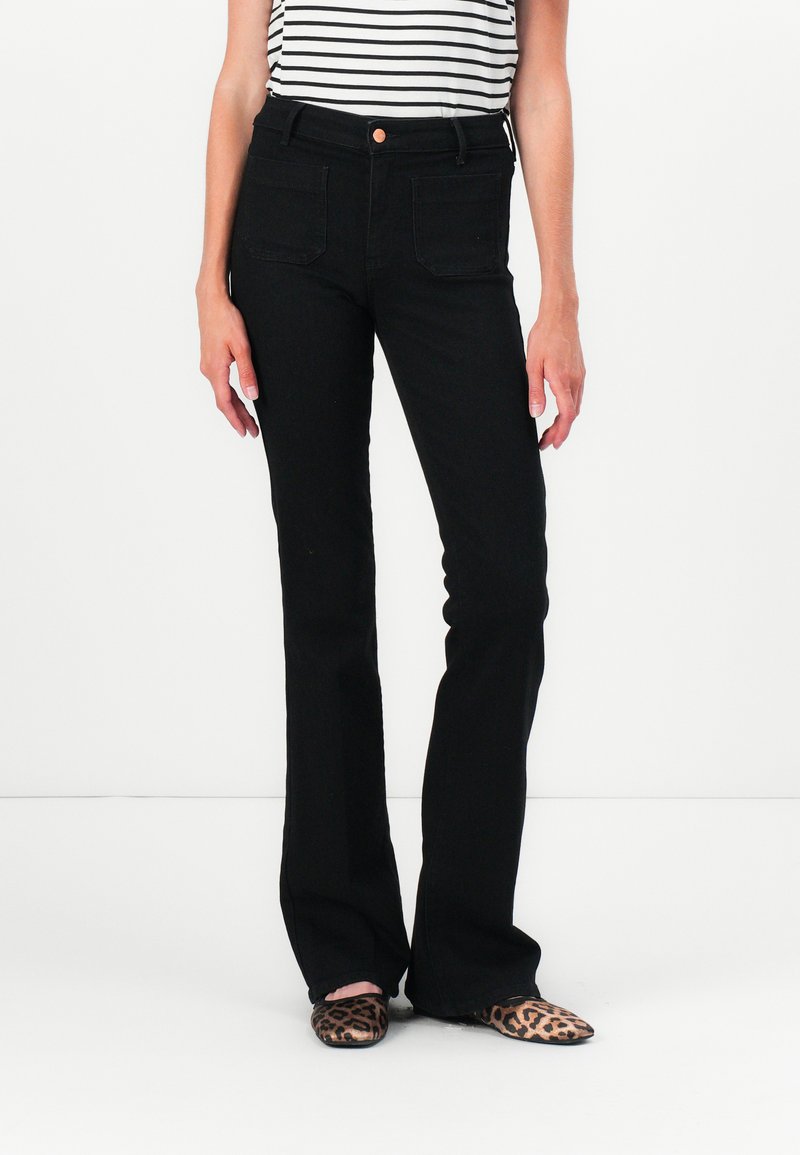 Black flared jeans with a high waist, featuring two front pockets and a copper button detail. Worn with a striped top and animal-print shoes.
