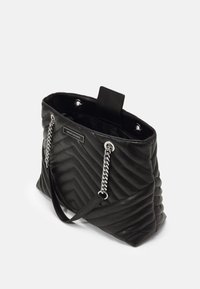 Czarna pikowana torba typu tote z uchwytami na łańcuszkach w srebrnym kolorze, ozdobiona teksturowanym wzorem w zygzak oraz kieszenią wewnętrzną. Zapięcie na klapę u góry.