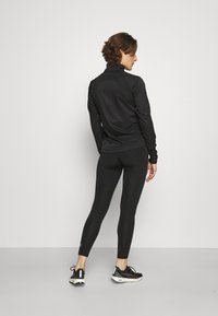 Schwarzes langärmliges Sportoberteil mit hohem Kragen, kombiniert mit eng anliegenden schwarzen Leggings und Laufschuhen. Glattes Material, minimalistisches Design.