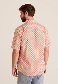 Korte mouwen shirt in helder oranje met een geometrisch patroon in blauw, geel en rood. Beschikt over een kraag en een gebogen zoom.