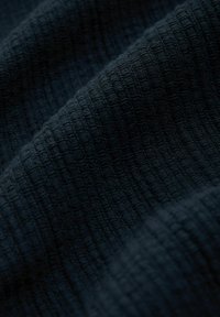 Tejido oscuro texturizado con un patrón de cuadrícula, que presenta tejidos elevados que crean una superficie táctil. La suavidad y la profundidad son evidentes en los pliegues.