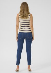 Débardeur en tricot avec des rayures marine sur un fond crème, associé à un jean foncé ajusté, doté de poches arrière et d'une silhouette slim.