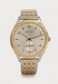 Kellon hopeinen ja kultainen ruostumattomasta teräksestä valmistettu kello, jossa on pyöreä kellotaulu, teksturoitu näyttö ja kolme alikellotaulua; siinä on rohkeat tuntimerkit ja kaksivärinen ranneke.