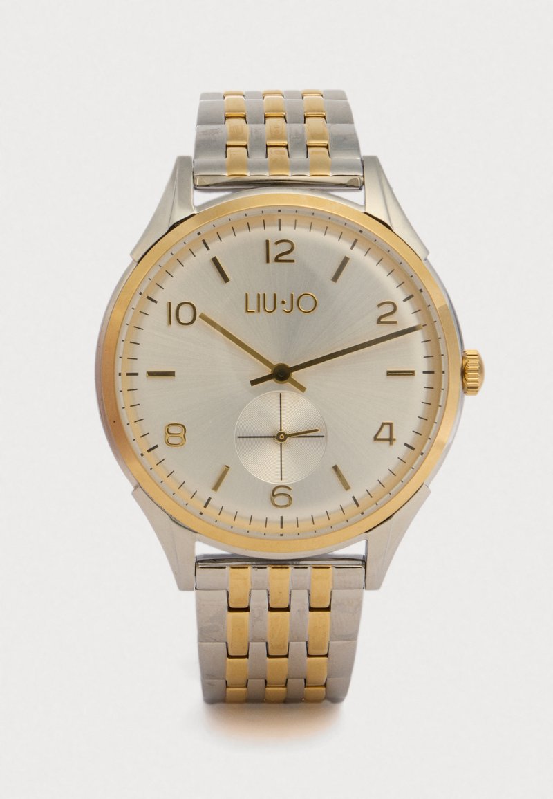 Kellon hopeinen ja kultainen ruostumattomasta teräksestä valmistettu kello, jossa on pyöreä kellotaulu, teksturoitu näyttö ja kolme alikellotaulua; siinä on rohkeat tuntimerkit ja kaksivärinen ranneke.