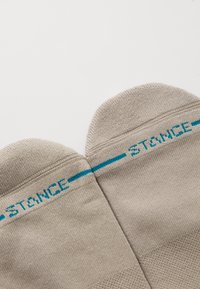 Beige crew socks with a smooth texture, featuring a light blue "STANCE" logo and horizontal stripes across the top.