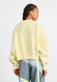 Felpa gialla oversize con scollatura a girocollo, polsini e orlo a costine. Abbinata a pantaloni grigi con accenti neon e motivo diagonale.