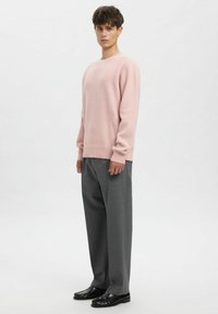 Lichtroze gebreide trui met ronde hals, lange mouwen, gecombineerd met antracietgrijze wijde broekspijpen en zwarte loafers. Soepele textuur.