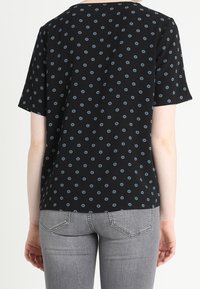 Haut noir à manches courtes avec un petit motif floral bleu, col rond et coupe décontractée. Associé à un jean gris clair.