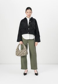 Donna che indossa una giacca nera con frange sopra una camicia bianca, pantaloni verde oliva, scarpe nere con punta, tenendo una borsa con motivo serpe.