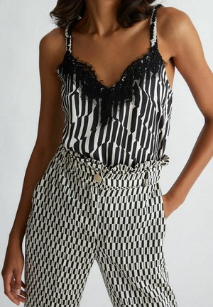 Mujer con camisola de rayas blancas y negras con ribete de encaje negro y pantalones de talle alto a cuadros blancos y negros con cinturilla fruncida.