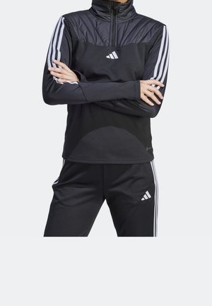 Top atletico nero con colletto alto, sezione superiore imbottita e strisce bianche lungo le maniche. Il tessuto è liscio e aderente.