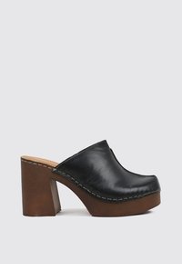 Zueco de cuero negro tipo slip-on con una gruesa suela de plataforma de madera marrón y tacón alto grueso sobre un fondo claro.