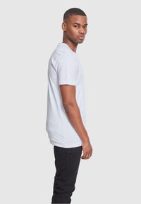 Witte t-shirt met korte mouwen, gemaakt van katoen, met een ronde hals en een rechte pasvorm. Draagt met zwarte broek, zijaanzicht.