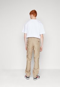 Beige cotton cargo pants with a relaxed fit, featuring back pockets and a belt loop, paired with a plain white t-shirt and black sneakers.