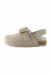 Sabots en suède beige avec une sangle et une boucle dorée, dotés d'une semelle en liège. La vue de côté met en avant leur style décontracté et leur confort.