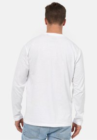 Langærmet hvid t-shirt lavet af bomuld, med en rund halsudskæring og en lige kant, båret med lyseblå denimbukser.