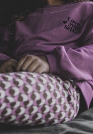 Sweatshirt violet avec le texte « Love your self », associé à des leggings roses et marron à motifs, présentant un design abstrait répétitif.