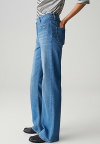 Brede blauwe spijkerbroek met een gemiddelde wassing, hoge taille en steekzakken. Heeft subtiele vervaging en een knoopsluiting.