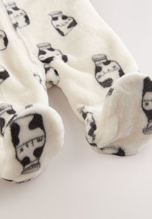 Fleece onesie in crème met zwart koeienprint en melkkanmotieven, met een zachte textuur en gesloten voeten voor warmte.
