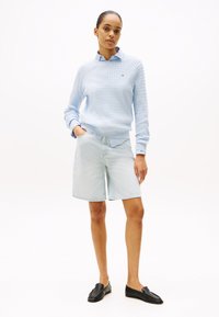 Lichtblauwe gebreide trui met een ronde halslijn, gecombineerd met licht denim shorts en zwarte instappers. Opvallende textuur en een relaxte pasvorm.