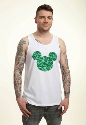 Biały top na ramiączkach z zielonym wzorem sylwetki Myszki Mickey w kwiaty. Modelka ma tatuaże i nosi szare dżinsy.