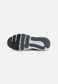 Shoe sole with a predominantly black rubber traction pattern, raised circular and oval details, bordered by a white midsole.