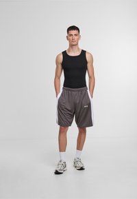 Czarna koszulka na ramiączkach zestawiona z szarymi szortami z białymi bocznymi panelami i wiązanym pasem. Sportowe buty dopełniają outfit.