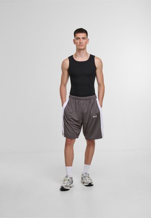 Schwarzes Tanktop kombiniert mit grauen Shorts, die weiße Seitenstreifen und einen Kordelzugbund haben. Sportliche Schuhe runden das Outfit ab.