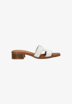 Sandal de deslizamiento blanco con una correa curva que presenta recortes abiertos, sobre una plantilla texturizada en tono marrón y un tacón bajo y cuadrado.
